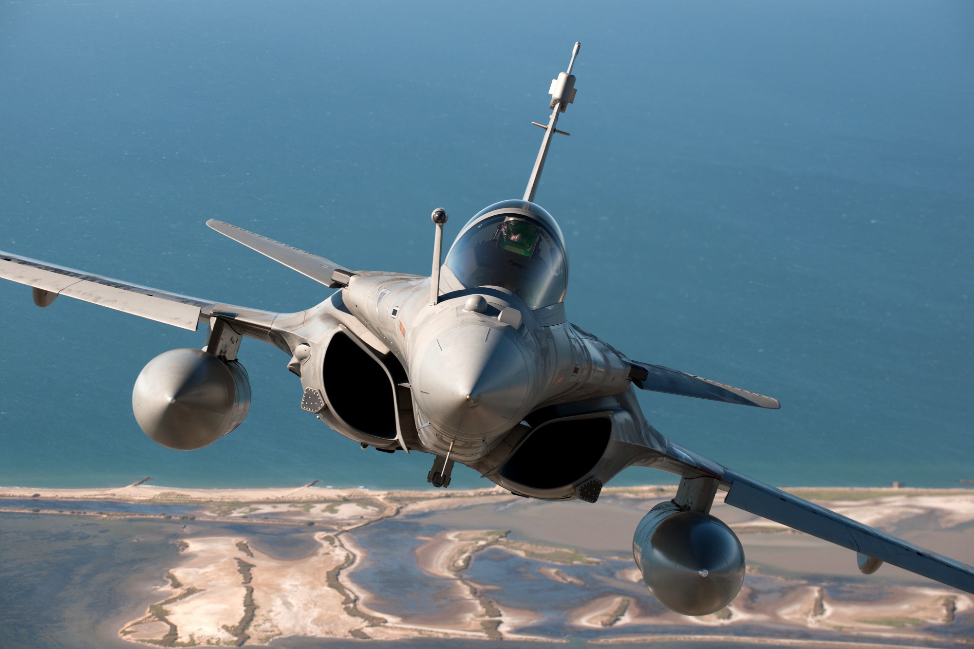 Caça Rafale em voo de patrulha sobre área costeira, destacando alcance tático da aeronave